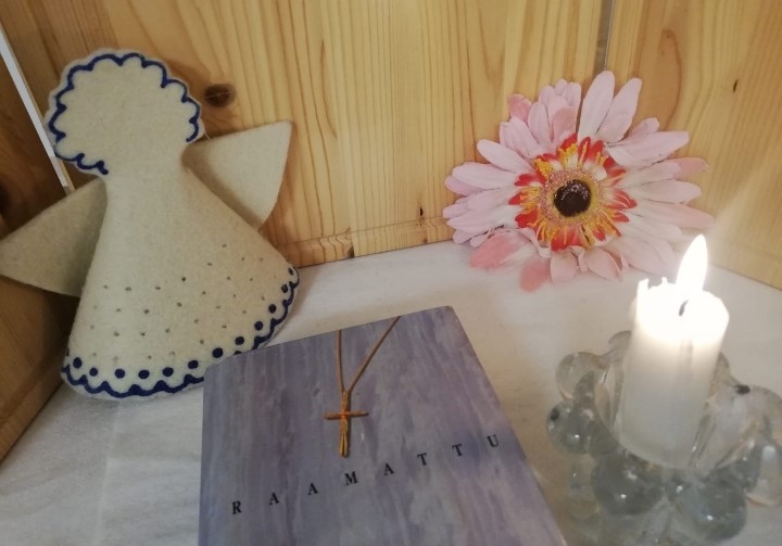 Alttari, jossa raamattu, kukka, enkeli ja kynttilä.